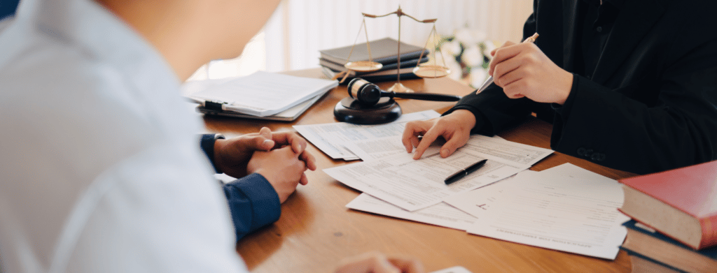 people sitting across each other at desk with only hands showing and papers on desk with gavel