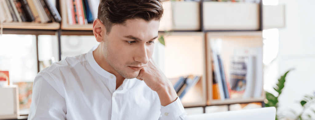 man with white shirt sitting with hand on chin