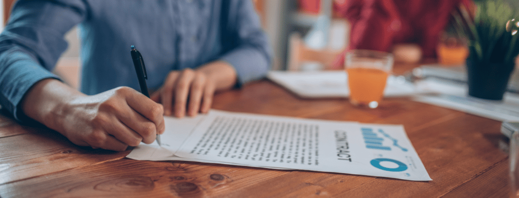 person's hands signing a contract with pen on a desk