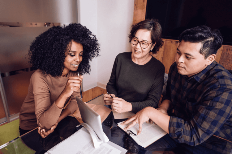 three people looking at tablet screen and discussing paperwork