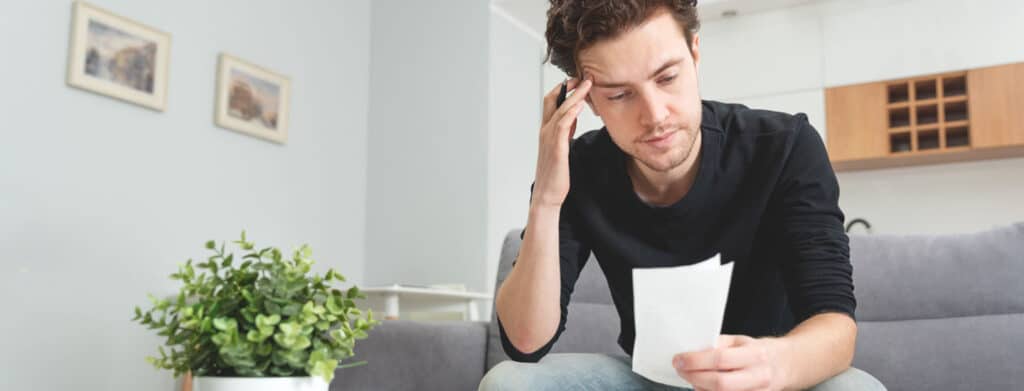 white man sitting on couch looking at piece of paper and thinking