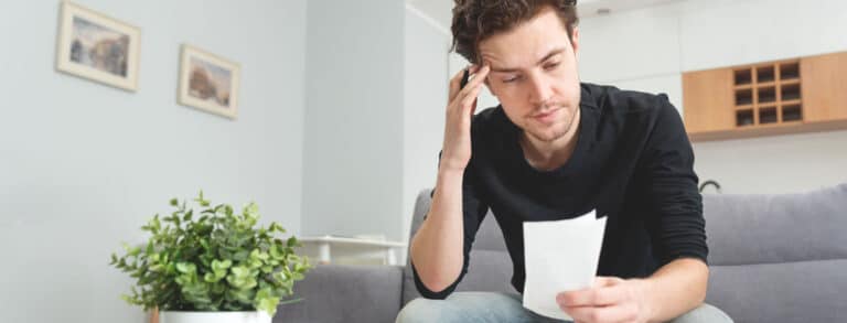 white man sitting on couch looking at piece of paper and thinking